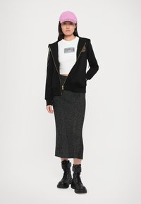 Black zip-up hoodie with gold accents, white crop top, gray knitted long skirt, and black lace-up boots. Pink cap completes the outfit.