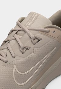 Nærbilde av beige Nike-sneaker med teksturert stoff, matchende lisser og synlig swoosh-logo på siden.