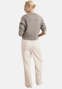 Grijze gebreide trui met opgerolde mouwen, gecombineerd met crèmekleurige broek met dunne verticale strepen. Eenvoudige, relaxte pasvorm, gladde textuur.