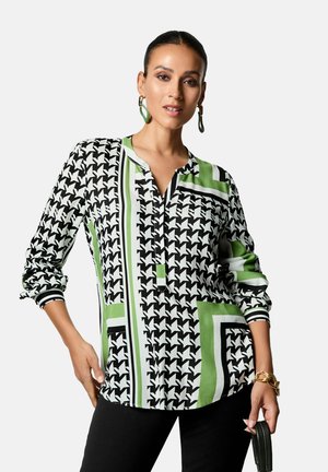 Zwart-wit geblokte blouse met groene accenten, voorzien van een knoopsluiting bij de hals en lange mouwen. Getextureerde stof met duidelijke randen.