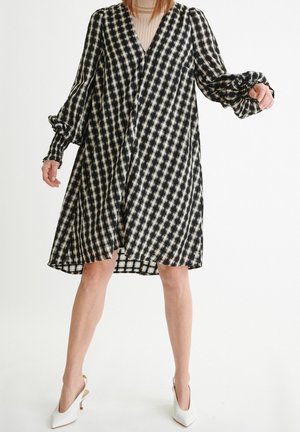 Robe à carreaux noir et blanc avec de longues manches bouffantes, un décolleté en V profond, une coupe ample et une longueur au genou. Tissu léger et aéré.