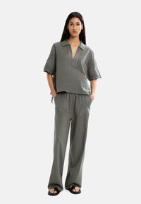 Completo grigio composto da due pezzi, caratterizzato da una camicia corta con colletto e maniche corte e pantaloni dal taglio ampio con tasche laterali e una silhouette rilassata.