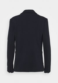 Blazer azul marino oscuro con hombros estructurados, abertura trasera simple y cuatro botones en los puños. Hecho de tejido suave, ajuste entallado.
