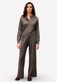 Ensemble de loisirs en tricot gris comprenant un haut à col et manches longues avec des boutons, ainsi que des pantalons à jambes larges. Le tissu a une texture douce.