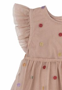 Ärmlös beige klänning med volangfåll i nät vid axlarna och flerfärgade glittriga prickar spridda över tyget.