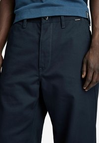 Donkerblauwe broek met een rechte pasvorm, gemaakt van slijtvast materiaal. Voorzien van versterkte stiksels, een knoopsluiting en een subtiel merkembleem.