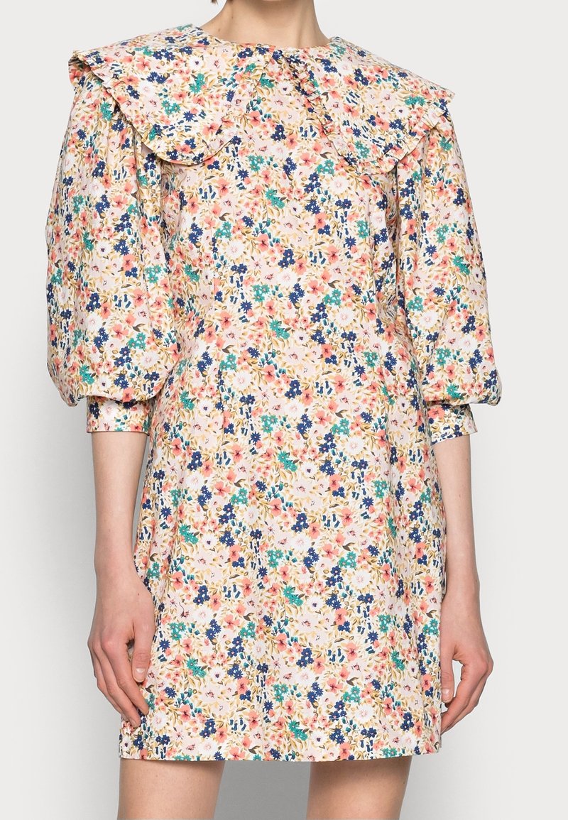 Robe mini florale avec des manches bouffantes trois-quarts et un large col volanté dans des couleurs pastel de rose, bleu, vert et blanc.