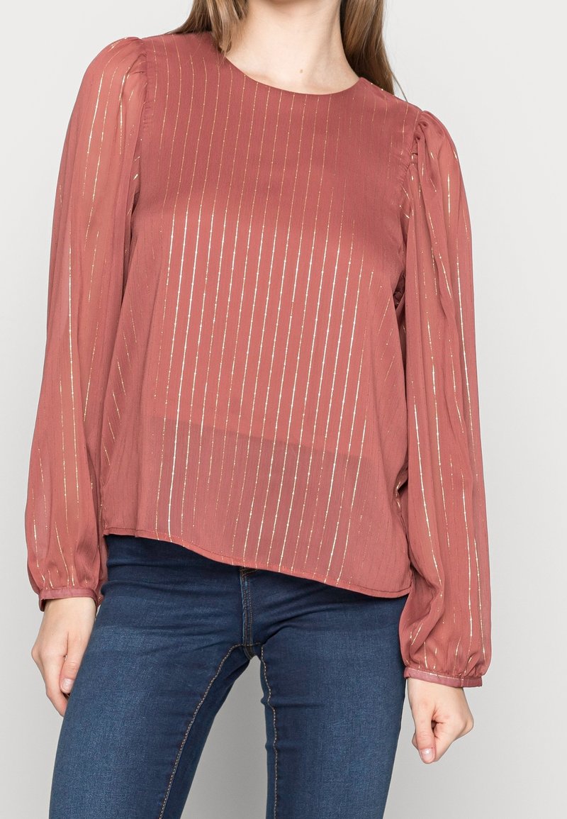 Blusa color óxido con mangas largas y voluminosas, con rayas verticales metálicas y cuello redondo; fabricada en una tela ligera y texturizada.