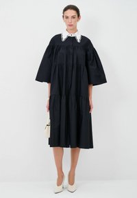 Abito nero a strati con maniche corte e larghe e colletto bianco con cuciture decorative. Tessuto liscio, design al ginocchio e stile minimalista.