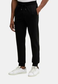 Svarta träningsbyxor med en texturerad sidopanel, elastisk midja och uppvikta anklar, kombinerade med vita sportskor.