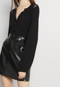 Blusa nera a maniche lunghe con scollo a V e chiusura con bottoni, abbinata a una mini gonna lucida in faux pelle di coccodrillo nera.