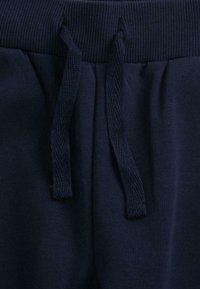 Un pantalon de survêtement bleu marine avec une taille côtelée et un cordon de serrage. Le tissu est lisse avec une texture mate et sans motifs visibles.