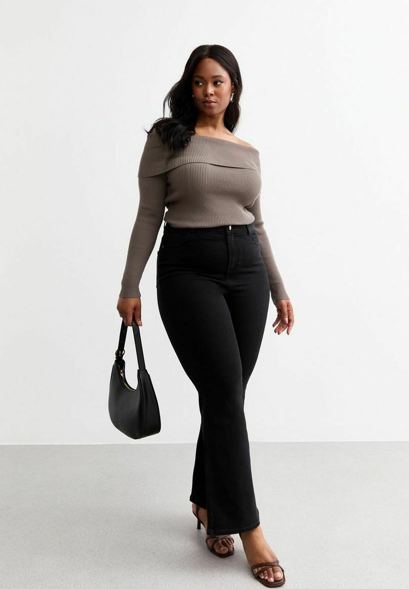 Maglione a spalla scoperta in rib di colore taupe, abbinato a jeans neri a vita alta e a campana, e sandali con tacco aperti neri; con una borsa nera.