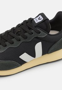 Sapatilhas em malha preta e camurça cinza, com um logo V branco, materiais texturizados e sola de borracha em tom creme. Design com atacadores.