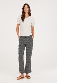 Hvid tekstureret kortærmet top kombineret med mønstrede sort-hvide løstsiddende bukser; modellen bærer brune strappy sandaler.