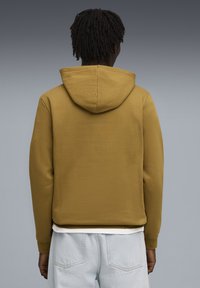 Felpa con cappuccio marrone dal morbido tessuto, dotata di tasca a marsupio e polsini a costine. Abbinata a pantaloni corti di jeans azzurri.