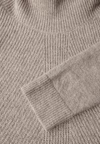Strickpullover in hellbeige mit einer gerippten Textur. Hoher Ausschnitt mit einem glatten Ärmelbund, der eine Mischung aus Strickmustern zeigt.