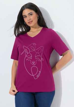 Mujer de cabello oscuro con una camiseta de cuello en V color magenta que tiene un dibujo de línea continua de un zorro sonriente y un pájaro.