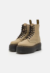 Stivali platform in pelle beige con lacci, suole spesse nere, cuciture gialle e linguette con logo su sfondo bianco.