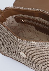 Woven béžová kabelka s texturovaným povrchem, obsahující vnitřní kapsu na zip a vzorovanou podšívku, zdobená zlatým knoflíkem na zavírání.