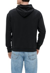 Sudadera negra con capucha ajustable, puños y dobladillo acanalados. La vista posterior muestra una tela suave y un corte holgado. Combinada con jeans de lavado claro.