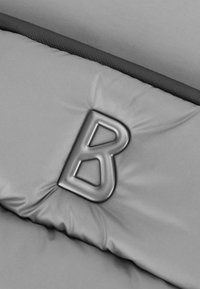 Grå vadderad tyg med en slät textur, som har en framträdande svart "B"-logotyp i en upphöjd design på ytan.