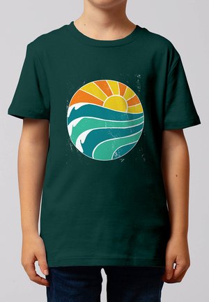 Kind trägt ein dunkelgrünes Shirt mit Grafik einer stilisierten Sonne und Ozeanwellen in einem Kreis auf der Vorderseite.