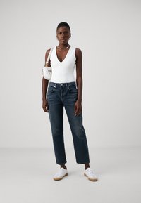 Un body sans manches blanc, un jean taille haute bleu marine et des baskets blanches avec des semelles beige. Le mannequin porte un petit sac à main blanc.
