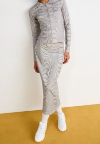 Grå ribbad långärmad tröja med krage och knappstängning, i kombination med en matchande figursydd kjol med vågmönster. Vita sneakers.