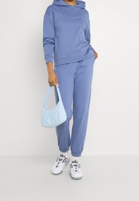 Ljusblå huvtröja och matchande joggers i mjukt material, kombinerat med en ljusblå handväska och vita sneakers.