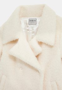 Cappotto crema con una texture pelosa, design doppiopetto, grande colletto a punta e bottoni bianchi. Interno foderato con etichetta del marchio.