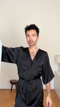 Μαύρο σατέν ρόμπα με μανίκια κιμονό και δέσιμο στη μέση. Λείο υφή, βαθύ V-λαιμόκοψη και ανταύγειες φωτός στον ύφασμα.