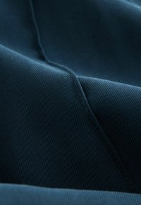 Donkerblauwe stof met een ribbeltextuur, voorzien van zichtbare stiksels langs de randen, wat gedefinieerde plooien en rondingen creëert.