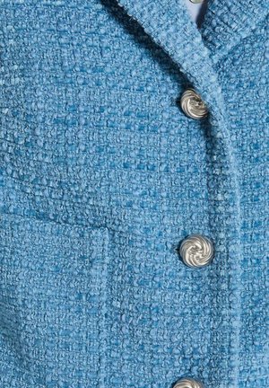 Blauer Tweed-Blazer mit strukturierter Oberfläche, ausgestatteter mit einem Reverskragen und silbernen Spiral-Knöpfen, einschließlich einem Detail mit Brusttasche.