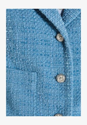 Blauwe tweedjas met een gestructureerd oppervlak, voorzien van een reverskraag en zilveren spiraalknopen, inclusief een detail van een borstzak.