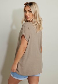 Maglietta beige oversize con maniche corte arrotolate, abbinata a pantaloni corti azzurri. Tessuto morbido con una leggera trama.