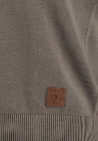 Maglione lavorato a maglia color marrone chiaro con orlo a coste testurizzato e una toppa in pelle marrone con logo in rilievo sul davanti.