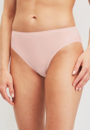 Buste et haut des cuisses d'une femme portant des sous-vêtements rose clair sans coutures, mains reposant près des hanches sur un fond uni.