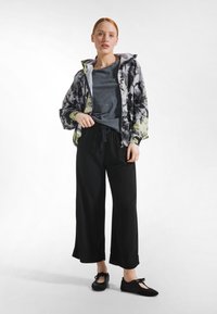 Jack met bloemmotief en capuchon, grijs gestructureerd shirt, losse zwarte broek en zwarte instappers met lintdetail.