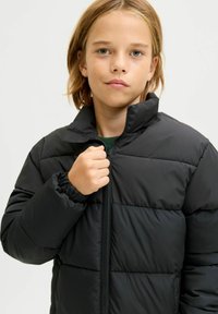 Svart dunjakke med glidelåslukking, elastiske mansjetter og quiltet tekstur. Designet har en ståkrage og en tettsittende passform.