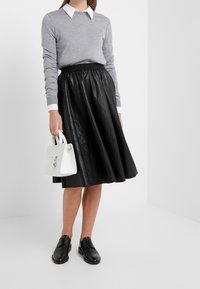 Šedý svetr s dlouhými rukávy a bílou košilí pod ním, doplněný černou koženou sukní ve tvaru A a černými šněrovacími botami. Bílá kabelka.