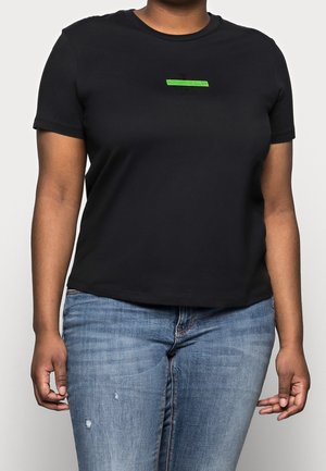 Osoba nosząca czarny t-shirt z krótkim rękawem z małym zielonym logo „Calvin Klein Jeans” oraz jasnoniebieskie postrzępione dżinsy.