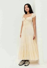 Maxi obleka iz svetlo rumene tkanine z nabranim prsnim delom, nabrano nes srajčki in večplastno krilo; v kombinaciji s črnimi in belimi čevlji.