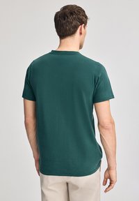 Camiseta de algodón de manga corta y cuello redondo en color verde oscuro. Textura suave con un acabado liso; diseño minimalista, sin logotipos ni acentos visibles.
