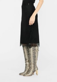 Knielange laarzen in metallic goud en zwart slangenprint, met een vierkante hak en decoratieve gouden accenten op de schacht.