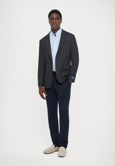 Sacou gri cu rever în formă de notch, asortat cu o cămașă cu dungi albastre și pantaloni navy. Loaferii bejeri completează ținuta.