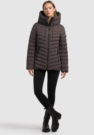 Gevoerde, capuchonjas in donkerbruin met diagonale gestikte textuur, rits aan de voorkant en zijzakken. Draag het met zwarte leggings en laarzen.