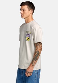 Lichtgrijs t-shirt met korte mouwen, ronde hals, met een meerkleurige grafische print op de linker borst. Katoenen stof, relaxte pasvorm.