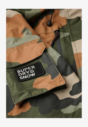 Tkanina w deseń kamuflażu w odcieniach zieleni i brązu. Posiada czarną prostokątną łatę z białym napisem "SUPERDRY SNOW".