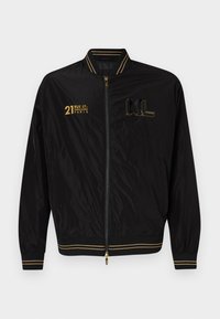 Black bomber jacket with gold accents, zip closure, ribbed cuffs and hem, featuring printed text and logos on the front. Smooth nylon material.